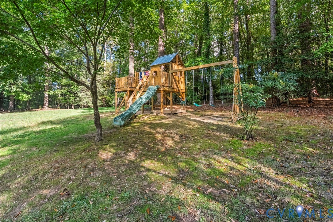 Expansive outdoor area featuring a wooden play structure with a slide, multiple swings, and mature surrounding trees