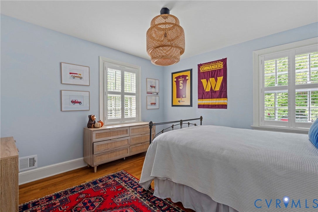 Hardwood flooring, two windows with plantation shutters, ceiling-mounted woven light fixture, and light blue wall color