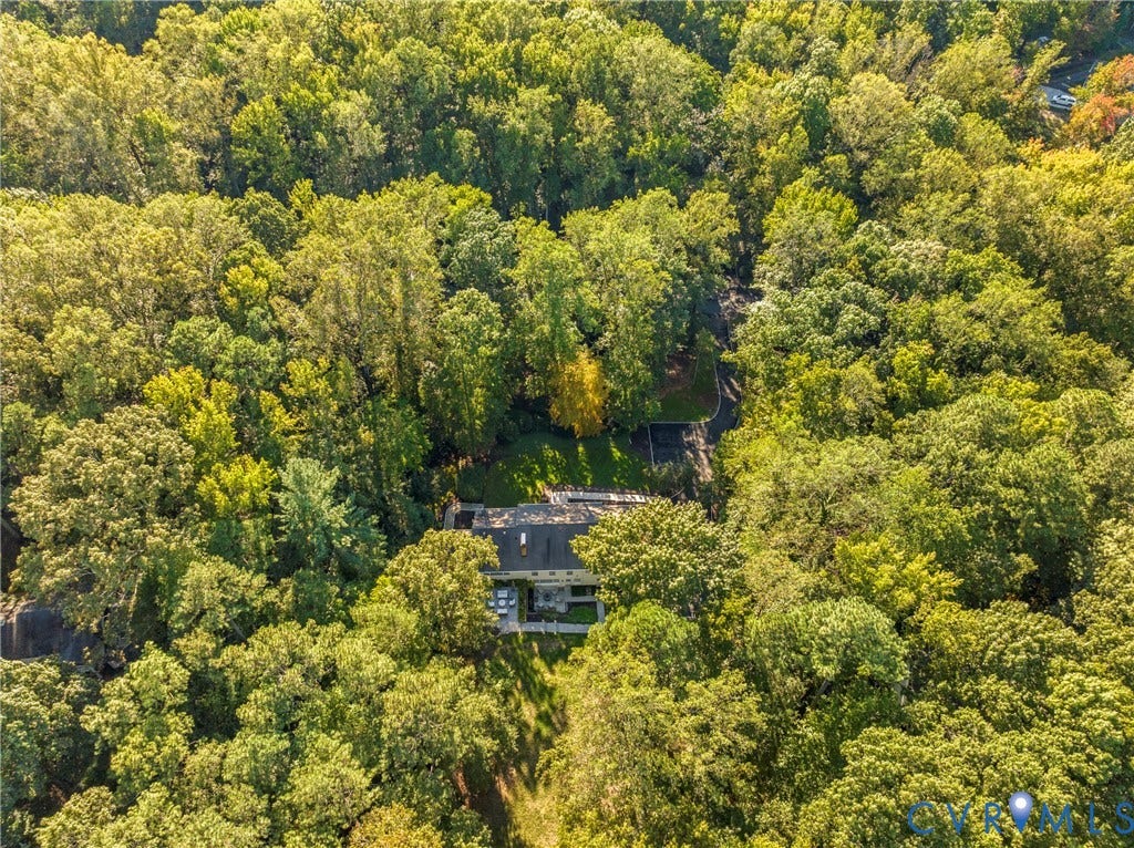 Aerial view of a property surrounded by mature trees, featuring a multi-level structure with a dark roof and a paved driveway