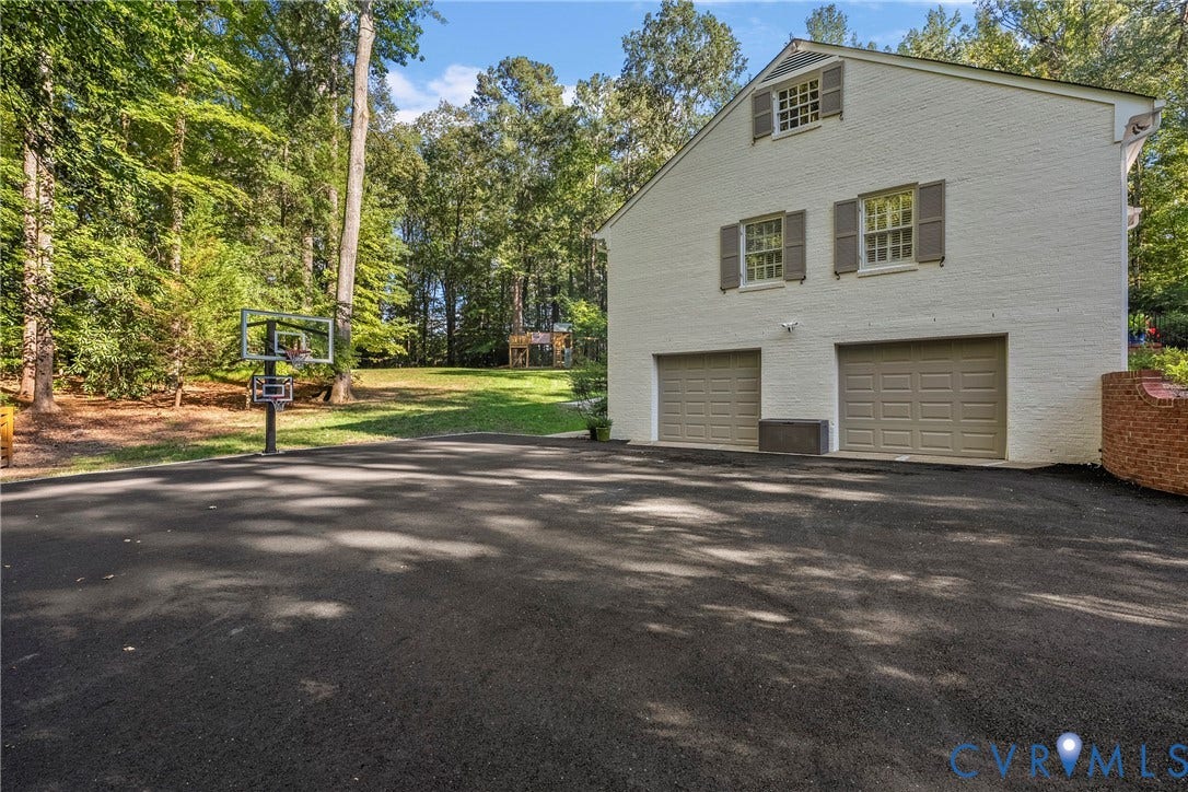 White brick exterior with two garage doors, dormer window, and a paved driveway