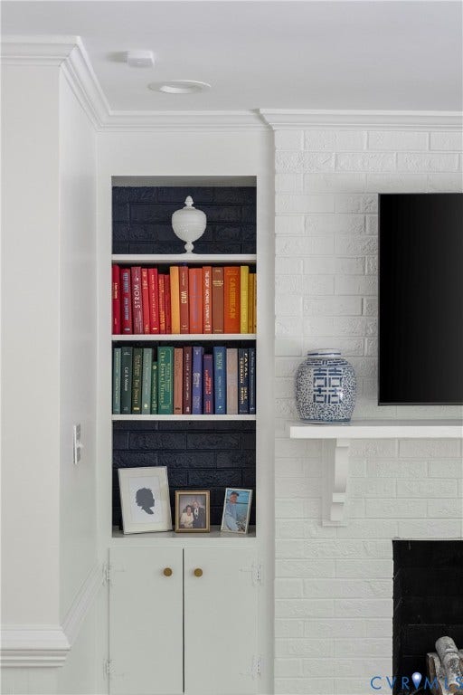 Built-in shelving with integrated cabinetry, crown molding, white brick fireplace surround, and recessed lighting