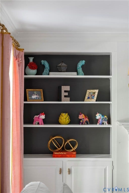 Built-in shelving with painted dark back panel, crown molding, and lower cabinetry with brass-finish hardware