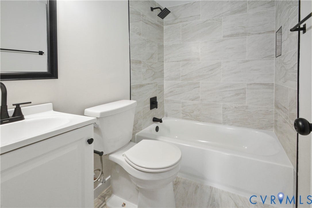 White vanity with integrated sink, black hardware, tile flooring, tile tub surround, and matte black fixtures