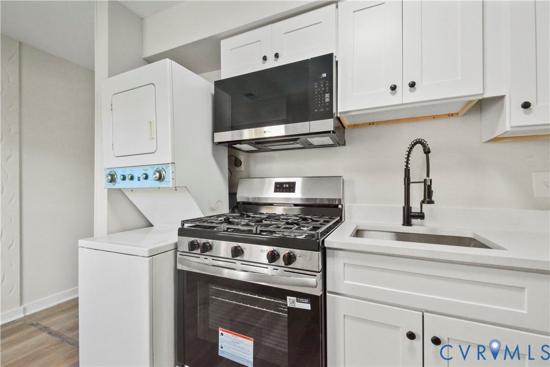 White shaker cabinetry, stainless steel range and microwave, stacked washer and dryer, and a single-basin sink with a matte black pull-down faucet