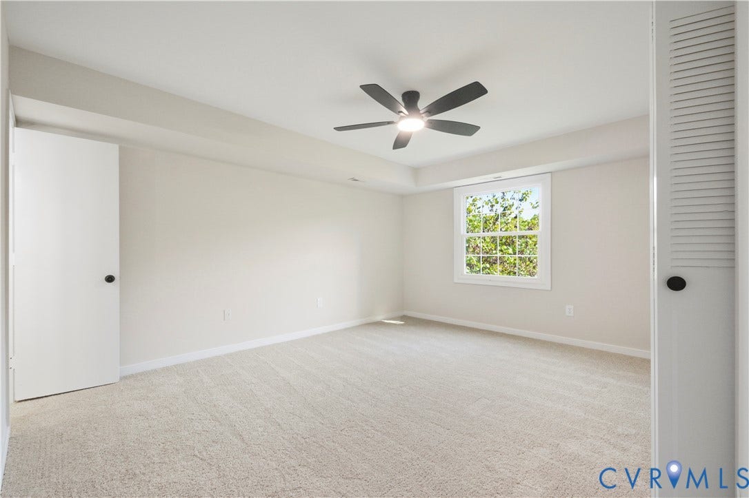 Carpeted room with a single window, a ceiling fan with integrated lighting, and a tray ceiling