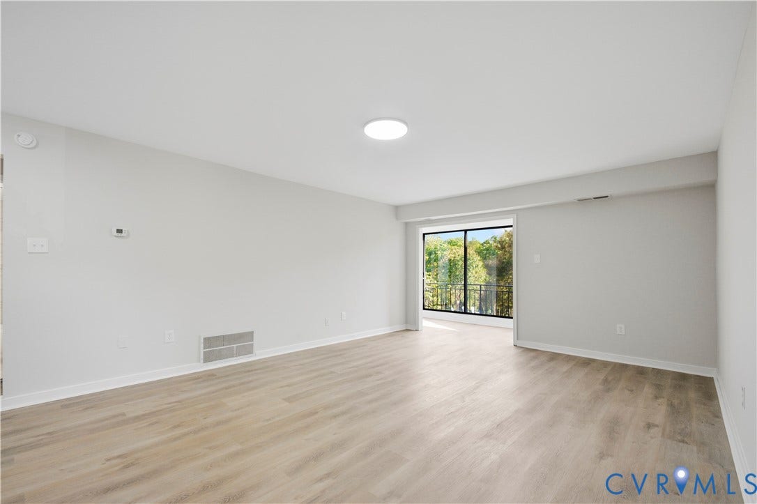 Light wood-finish flooring, white walls, and a large sliding glass door opening to a balcony with metal railing