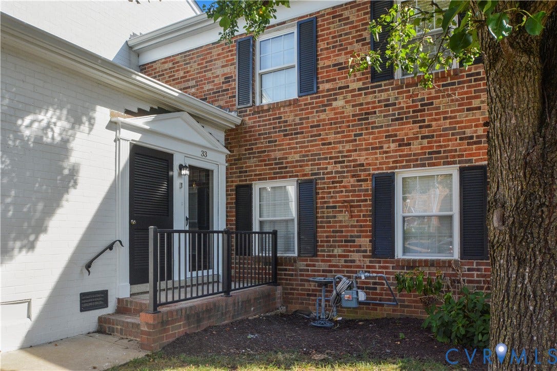 Brick exterior with white trim, featuring black louvered shutters and a covered entry with a decorative pediment