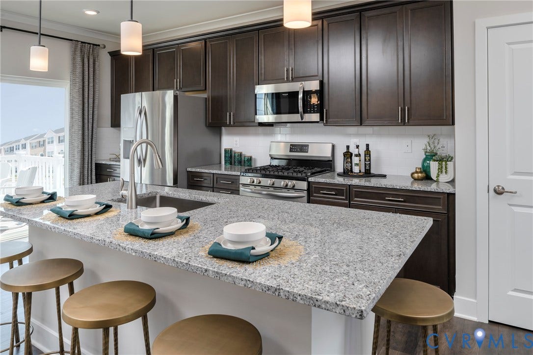 Kitchen featuring dark wood-finish cabinetry, stainless steel appliances, a white subway tile backsplash, and light-toned stone countertops