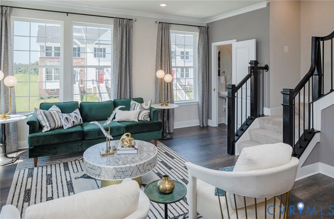 Expansive living area featuring large windows, wood-finish flooring, and a carpeted staircase with dark railings