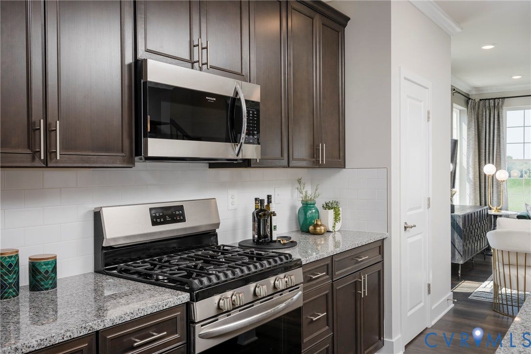 Dark wood-finish cabinetry, stainless steel range with gas burners, stainless steel built-in microwave, light granite countertops, and white subway tile backsplash