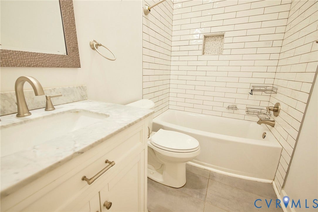 2421 Buena Vista Boulevard, Chester, VA 23831 White subway tile shower surround with an integrated niche, a white tub, a white vanity with a rectangular undermount sink, a stone countertop, and brushed nickel fixtures