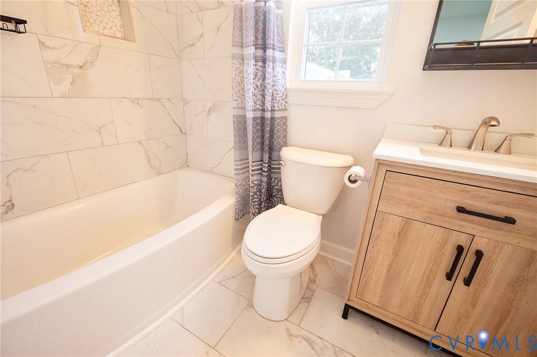 2421 Buena Vista Boulevard, Chester, VA 23831 White subway tile tub surround with a decorative niche, white bathtub, wood-finish vanity with a single basin sink, and a framed mirror