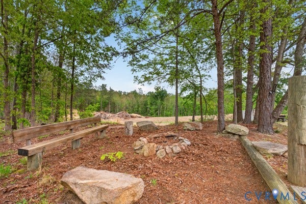 Outdoor fire pit area featuring a stone surround, natural wood benches, and mature trees