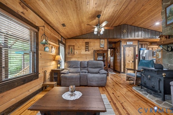 Wood walls and ceiling, vaulted ceiling, wood-finish flooring, ceiling fan, and stone fireplace with a wood-burning stove