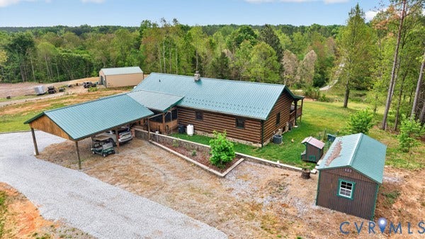 Log home with a green metal roof, a gravel driveway, an attached carport, and a separate storage shed