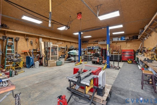 Spacious workshop featuring a concrete floor, built-in shelving, and overhead lighting. Car lift included