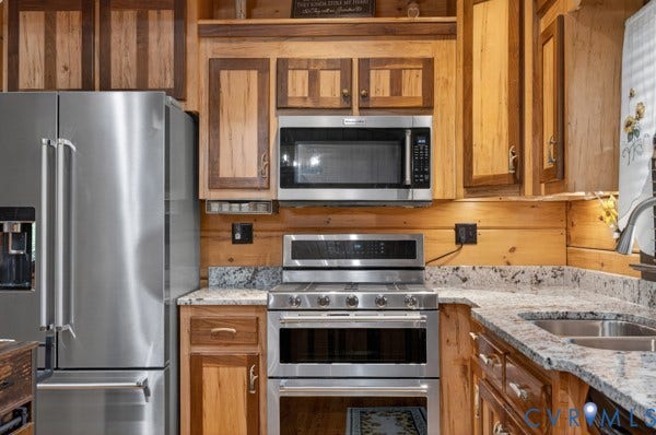 Stainless steel appliances, wood cabinetry, stone countertops, and a double oven range