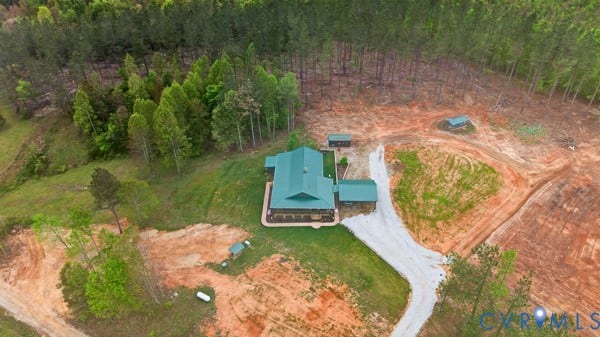 Property featuring a green metal roof, a gravel driveway, and surrounding wooded areas