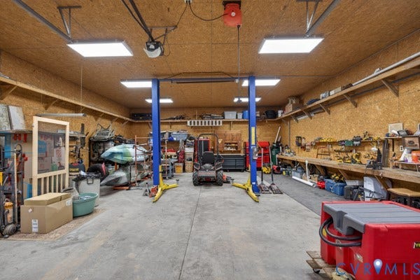 Spacious garage featuring a concrete floor, built-in shelving, two-post vehicle lift, and panel lighting