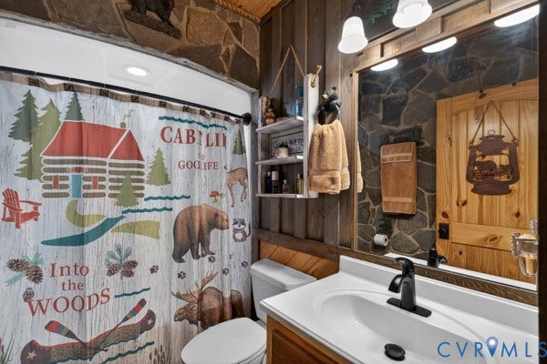2nd Bathroom featuring stone accent walls, a wood-paneled wall, a white vanity with an integrated sink, and a black-finish faucet