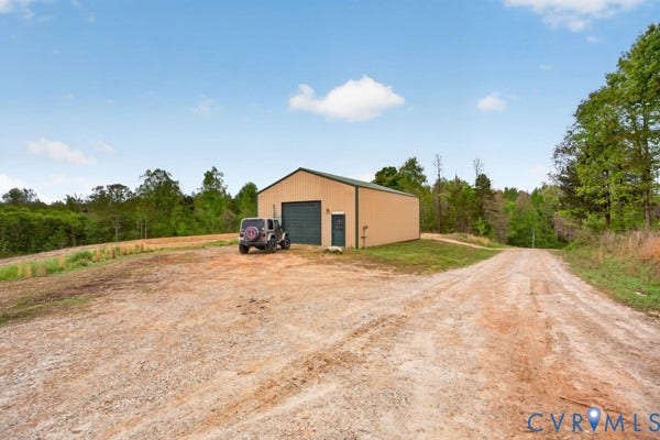 Metal outbuilding with a single overhead door, an entry door to shop and a gravel drive