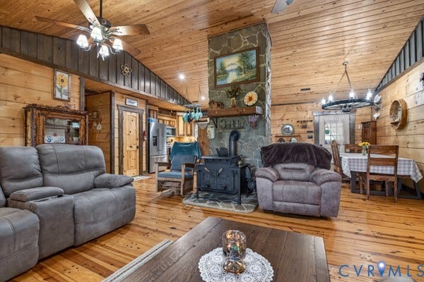 Vaulted wood ceiling, wood-finish flooring, stone-clad fireplace with wood-burning stove, exposed wood beam accents, and integrated ceiling fan with lighting