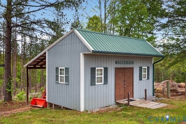 BUNKHOUSE: Light gray vertical siding with white trim, green metal roof, and a covered side porch