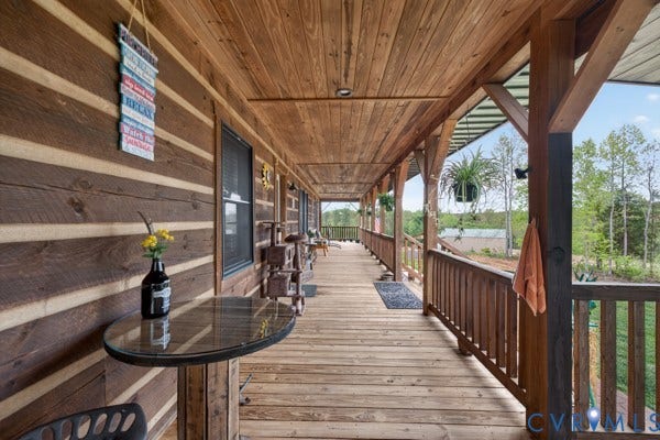 Expansive wood-planked porch with log cabin-style siding, wood railing, recessed lighting, and a durable metal roof