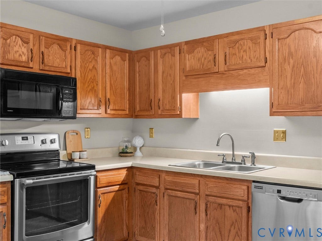 Kitchen featuring raised-panel oak cabinetry, stainless steel appliances, dual-basin stainless steel sink, and solid-surface countertops