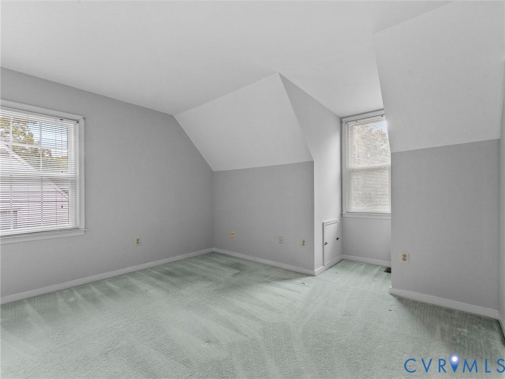 Neutral-toned room featuring angled ceilings, wall-to-wall carpeting, two double-hung windows, and a built-in knee-wall access door