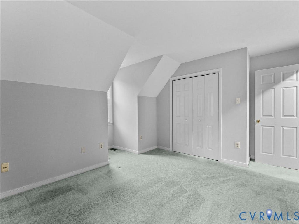 Interior room featuring vaulted ceilings, neutral wall tones, wall-to-wall carpeting, bi-fold closet doors, and a six-panel entry door