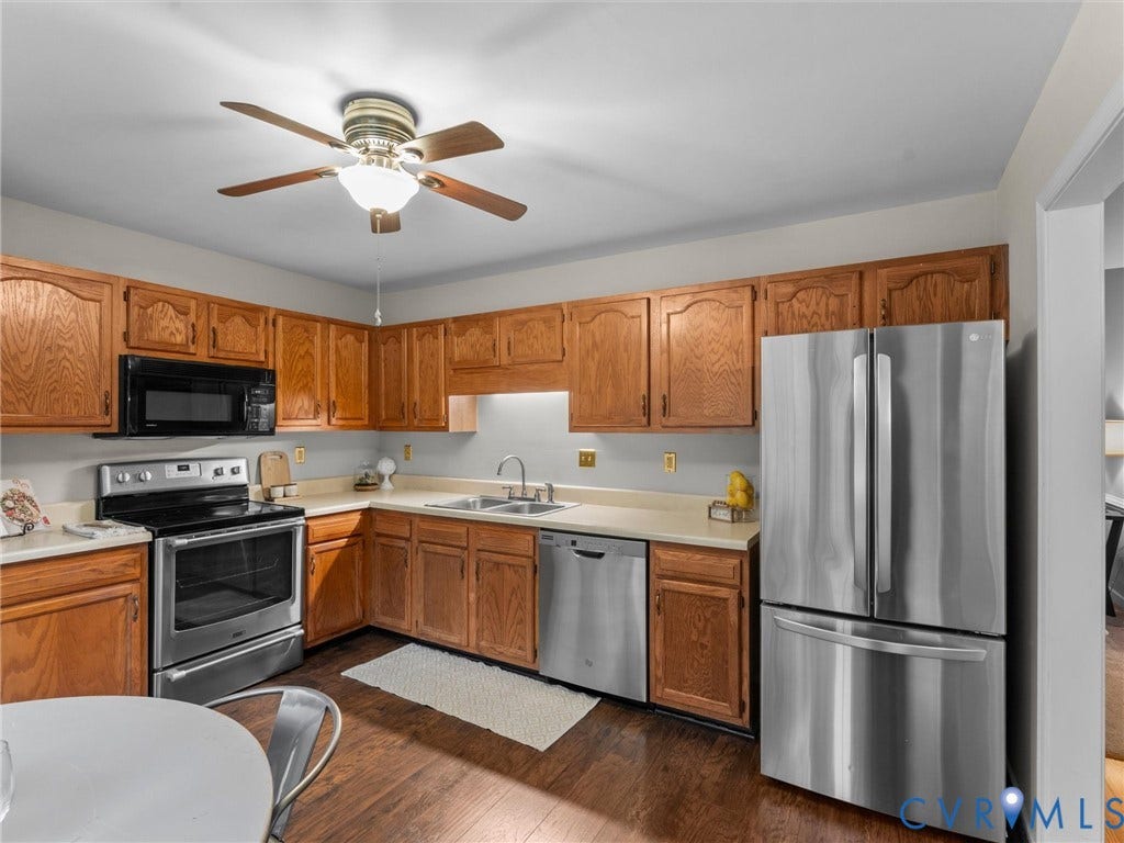 Kitchen featuring stained wood cabinetry, stainless steel appliances, solid surface countertops, dual-basin sink, and wood-finish flooring