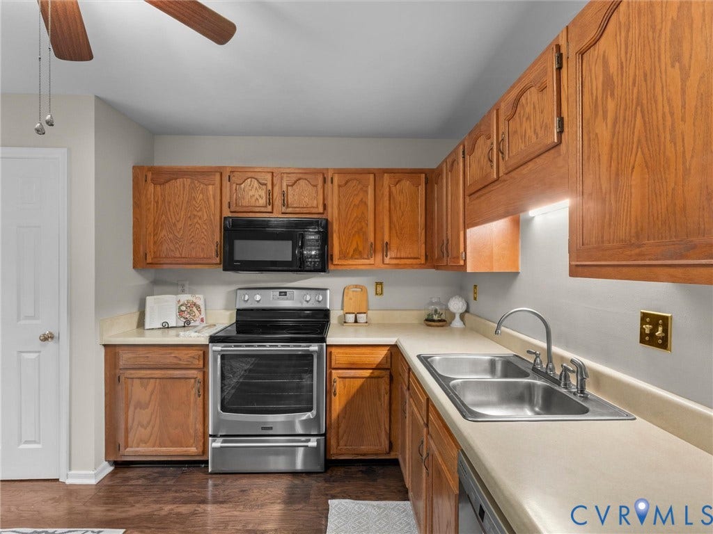 Kitchen featuring wood cabinetry, stainless steel appliances, solid-surface countertops, dual-basin stainless steel sink, and wood-finish flooring