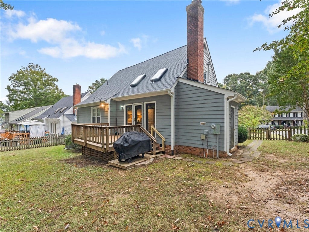 Exterior featuring blue siding, a multi-story brick chimney, dual roof skylights, a wood deck, and a fenced yard