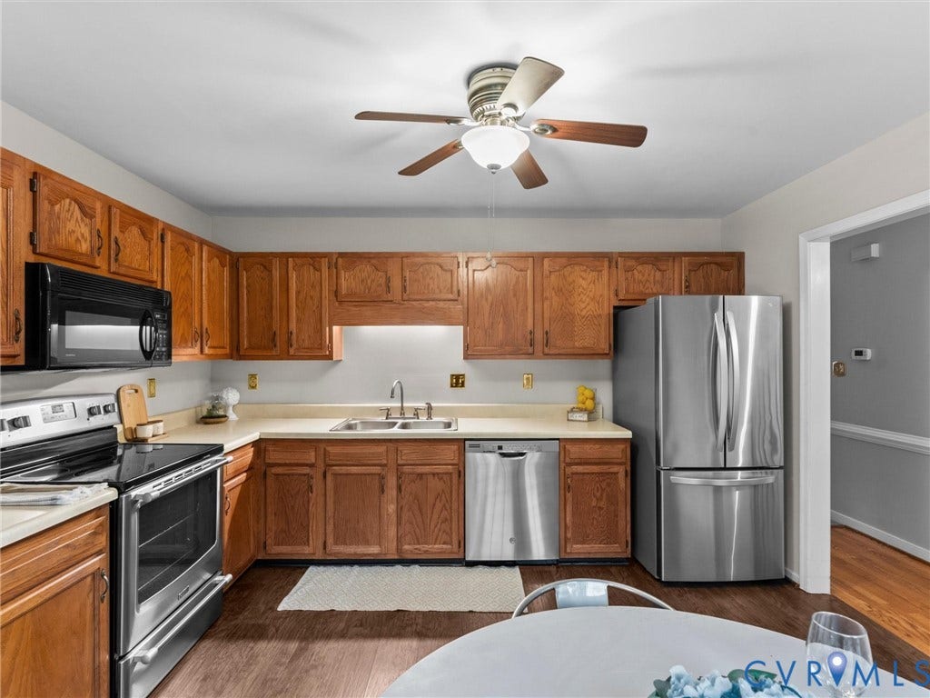 Kitchen featuring wood cabinetry, stainless steel appliances, dual-basin sink, and wood-finish flooring