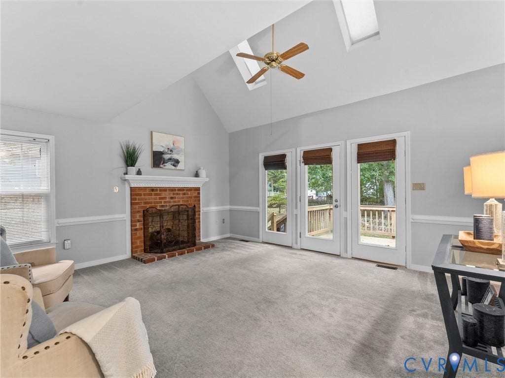 Vaulted ceilings featuring dual skylights, a brick-surround fireplace with a mantel, and three glass-paneled doors