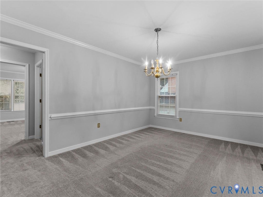 Interior space featuring crown molding, chair rail trim, wall-to-wall carpeting, and a multi-arm brass chandelier