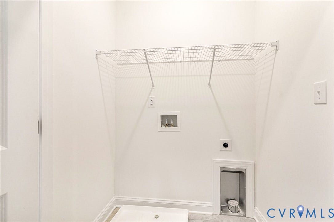 White wire shelving unit over laundry hookups, utility sink, and wall-mounted electrical outlets