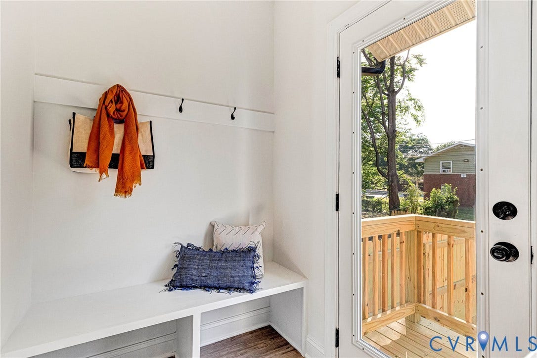 Built-in bench seating with cubby storage, wall-mounted coat hooks, wood-finish flooring, and a glass-paneled exterior door opening to a wooden deck with railings