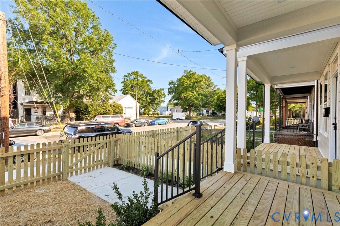 Expansive front porch with wood plank flooring, white support columns, and black metal railings