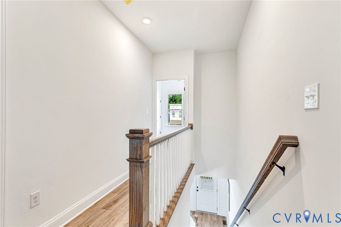 Recessed ceiling lighting illuminates a wood-finish flooring hallway with white walls