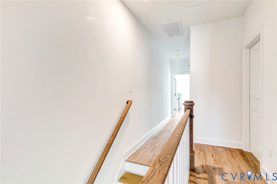 Hardwood-style flooring throughout, white wall finishes, natural wood stair railing, and a white interior door