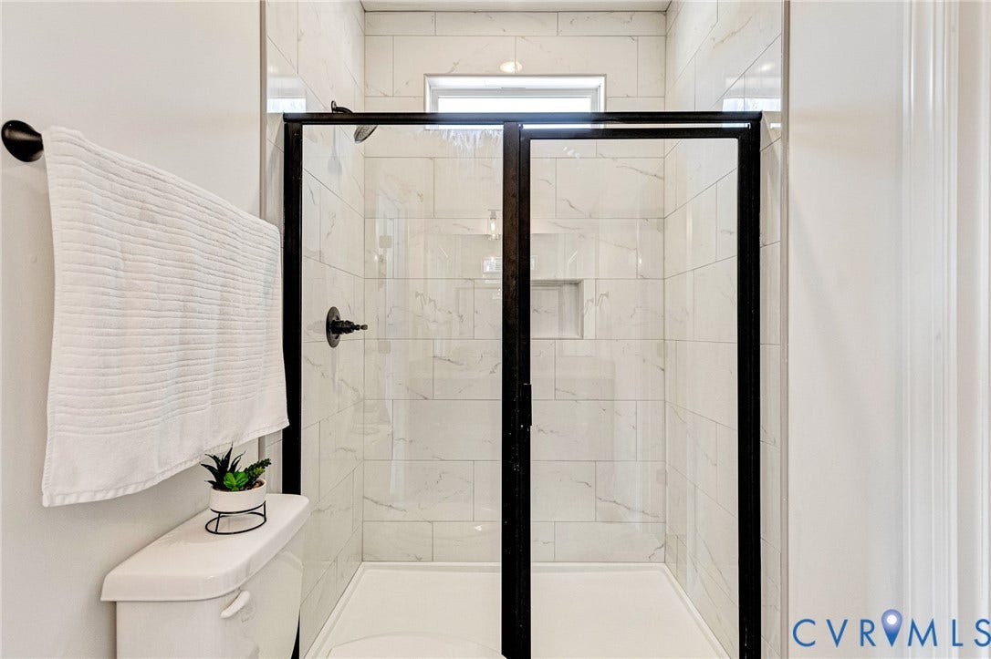 Frameless glass shower enclosure with matte black hardware, white subway tile shower surround, built-in shower niche, and a white shower pan