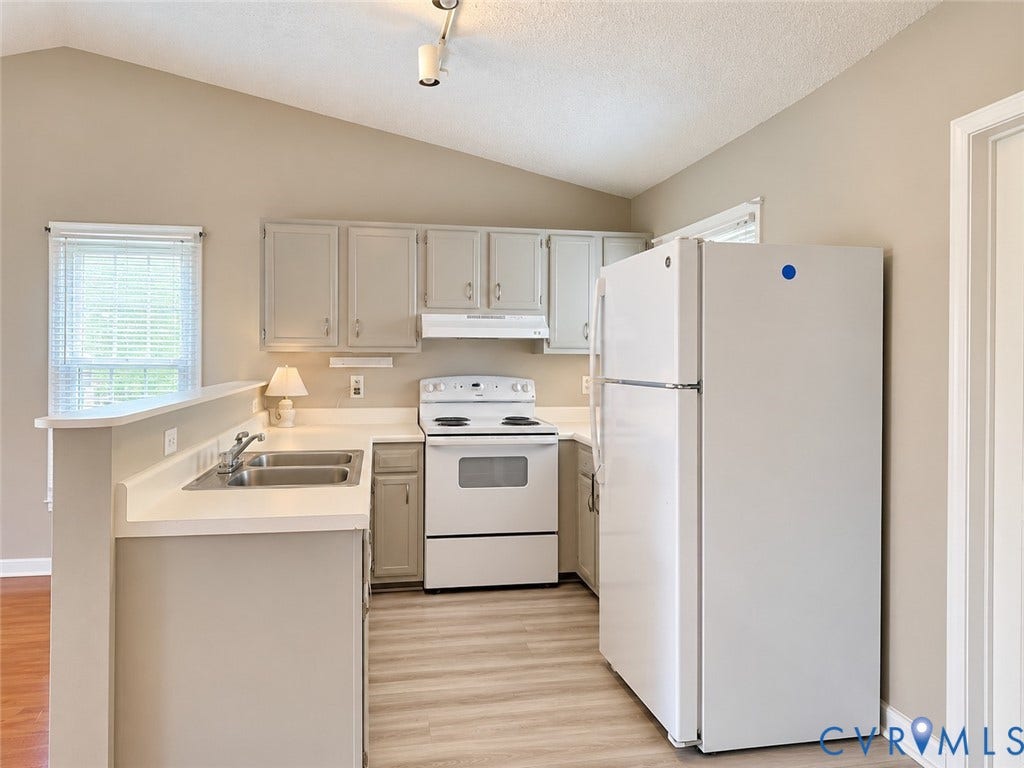 Henrico, VA 23223 Kitchen featuring cabinetry with shaker-style doors, solid-surface countertops, dual-basin stainless steel sink, wood-finish flooring, and vaulted ceiling