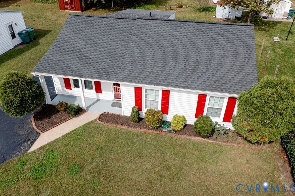 Henrico, VA 23223 Ranch-style residence featuring white siding, red window shutters, a dark shingle roof, a covered front porch with concrete flooring, and a landscaped front garden bed with a stone border