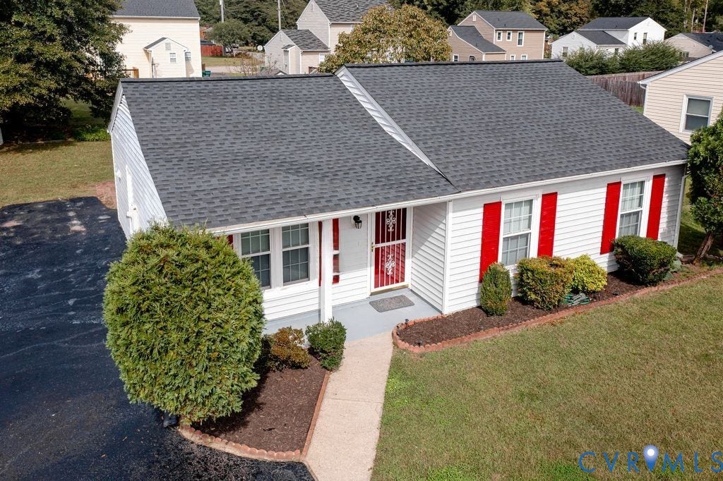 Henrico, VA 23223 Single-story residence featuring white siding, red window shutters, asphalt shingle roof, paved driveway, and landscaped garden beds with stone edging