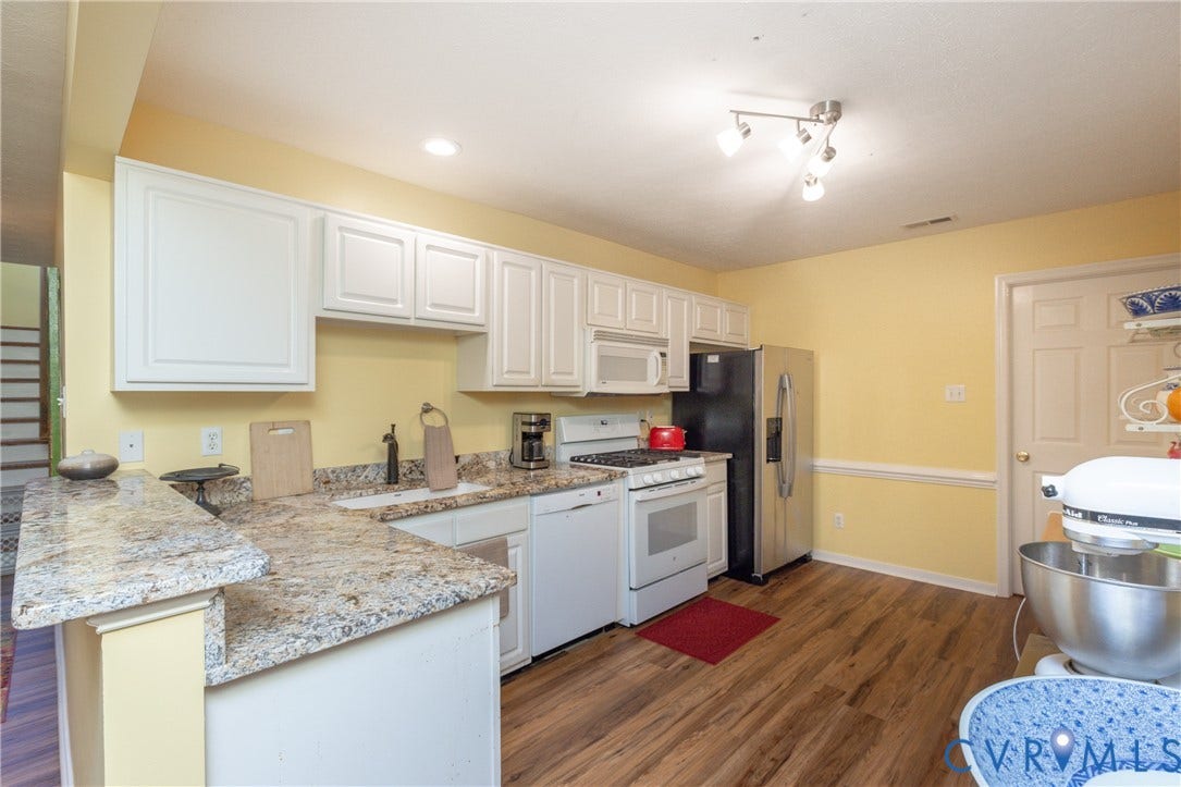 Kitchen featuring white cabinetry, light-toned countertops, wood-finish flooring, and a stainless steel refrigerator