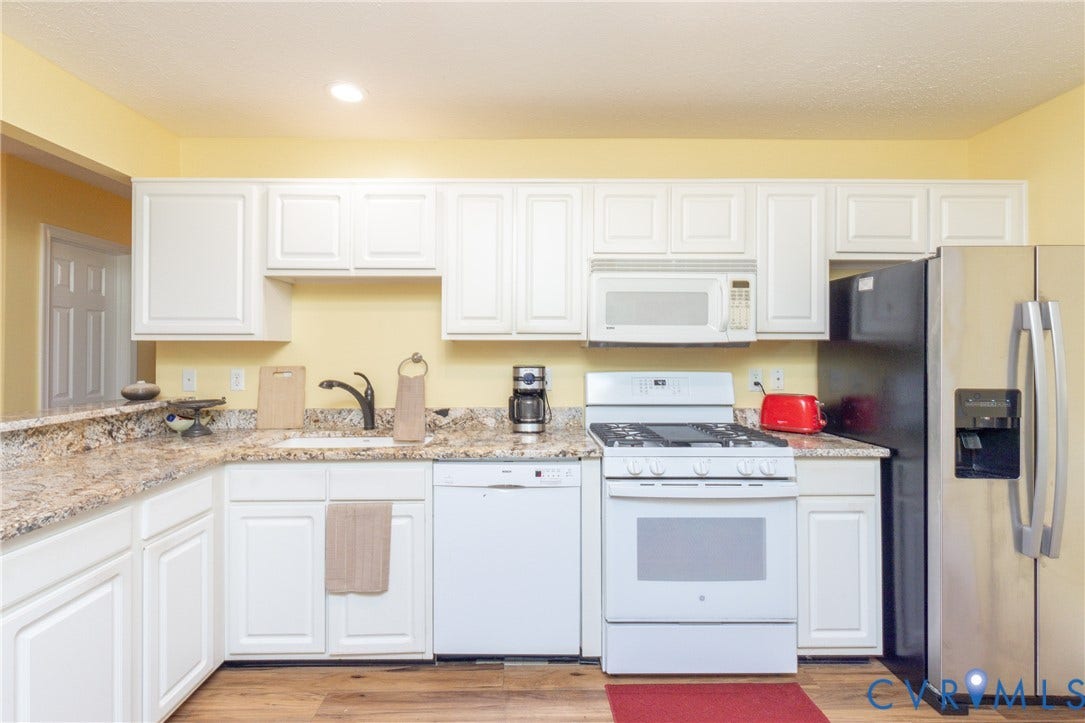 Kitchen featuring granite countertops, white cabinetry, a stainless steel refrigerator, white gas range, and wood-finish flooring