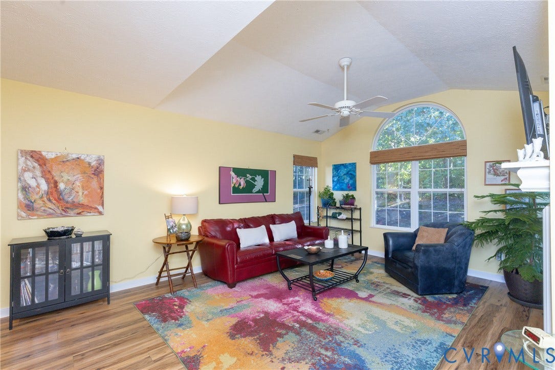 Vaulted ceiling with a ceiling fan, arched window, wood-finish flooring