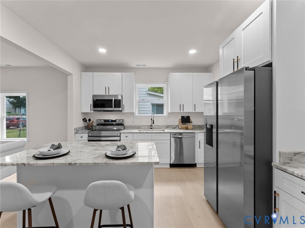 Open-concept kitchen featuring white cabinetry, stainless steel appliances, a kitchen island with seating, recessed lighting, and wood-finish flooring